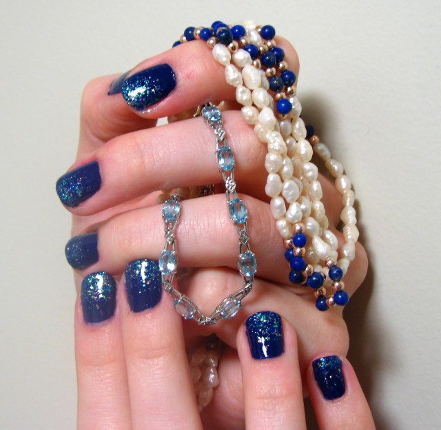 Syl's first attempt at nail art, displayed with some of the loot from Watersdeep, place that inspired this glittery blue manicure.